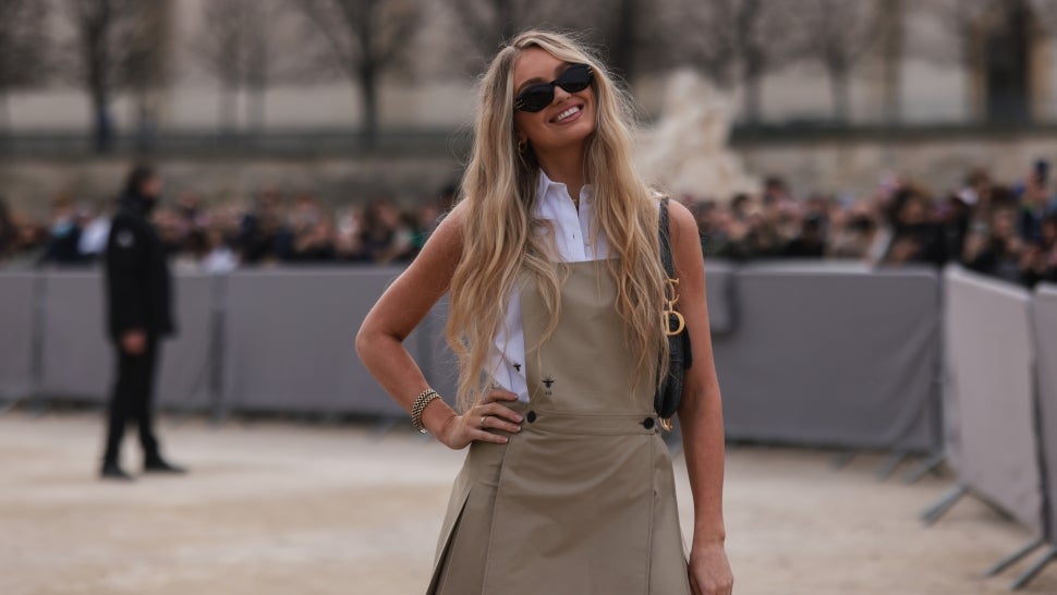Romee Strijd wears black sunglasses, a white sleeveless shirt, a beige tank-top / pleated short dress from Dior, a black embossed print pattern fabric shoulder bag from Dior, outside Dior, during Paris Fashion Week